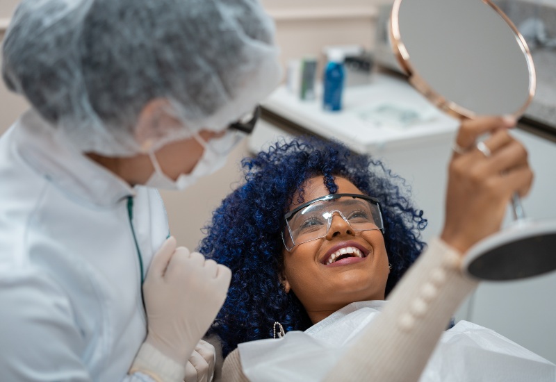 A happy patient examining results in a mirror after cosmetic dental treatments in Kenosha, WI